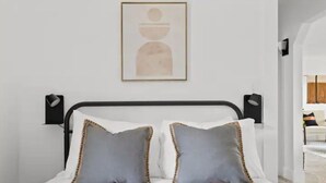 Et soveværelse med en seng, to puder, et indrammet kunstværk og et natbord med en lampe.