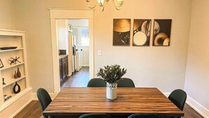 A dining area with a wooden table, four chairs, a potted plant, and three wall-mounted paintings. - Modern Comfort in a Bright Nampa Retreat (Nampa)