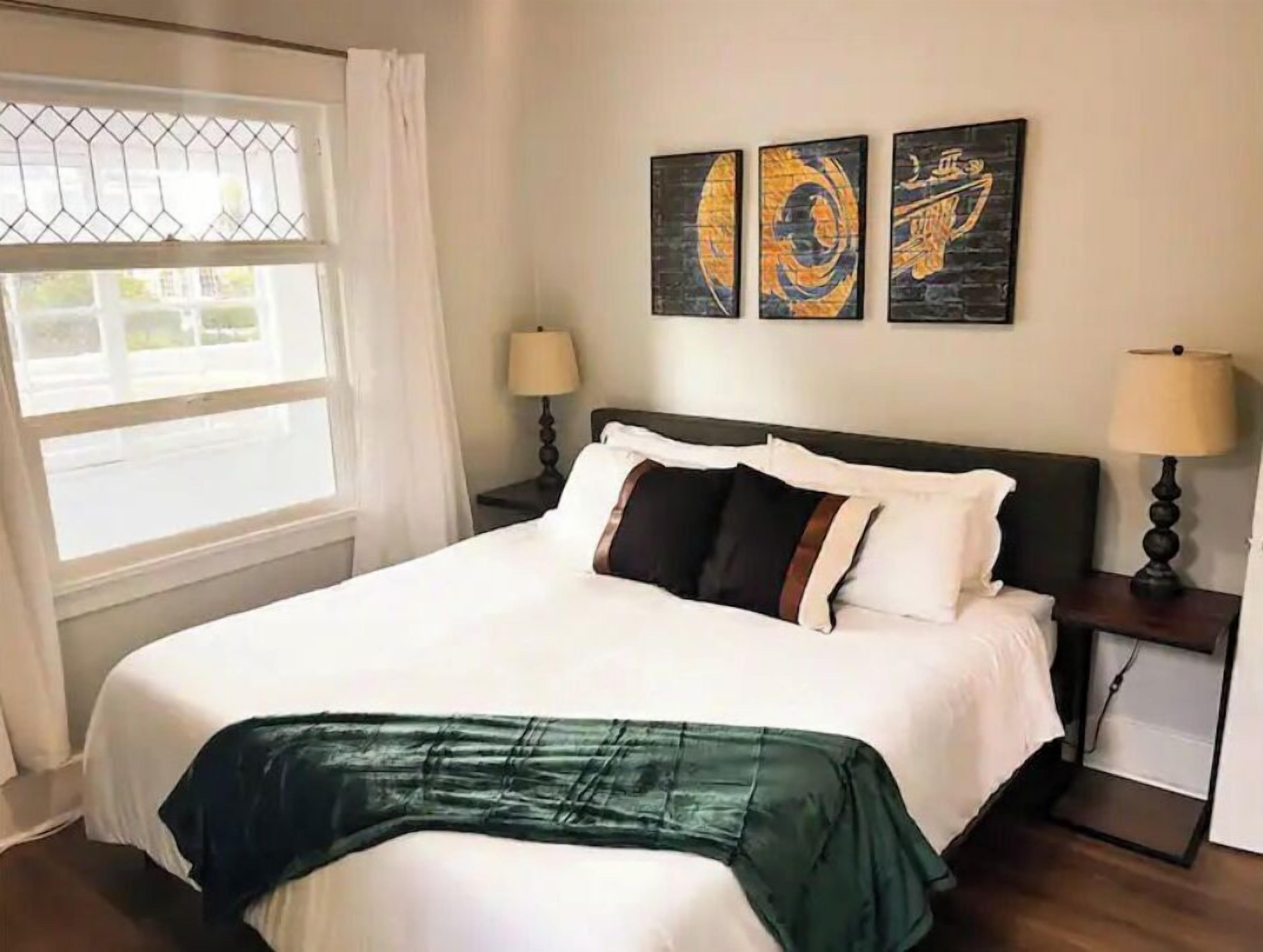 A neatly made bed with a green throw, two bedside lamps, and three artworks on the wall.
