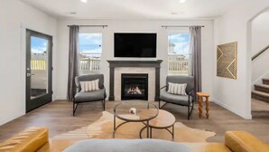 A modern living room with a fireplace, two armchairs, a coffee table, and a TV mounted above the fireplace. - New Modern Cozy Home in Meridian (Meridian)