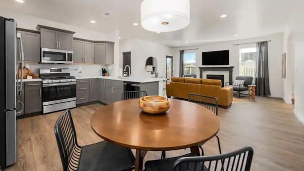A modern kitchen with grey cabinets, a microwave, and a stove. There is a dining area with a round table and chairs, and a living area with a sofa and a TV. - New Modern Cozy Home in Meridian (Meridian)