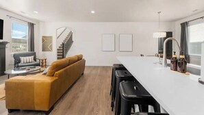 A modern living room with a sofa, a coffee table, and a dining area with bar stools. - New Modern Cozy Home in Meridian (Meridian)