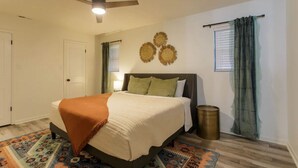 Un dormitorio con cama, ventilador de techo, ventana con cortinas y un adorno en la pared.