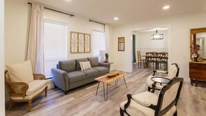 Una sala de estar con sofá, sillones, una mesa de centro y una zona de comedor con sillas y una araña.