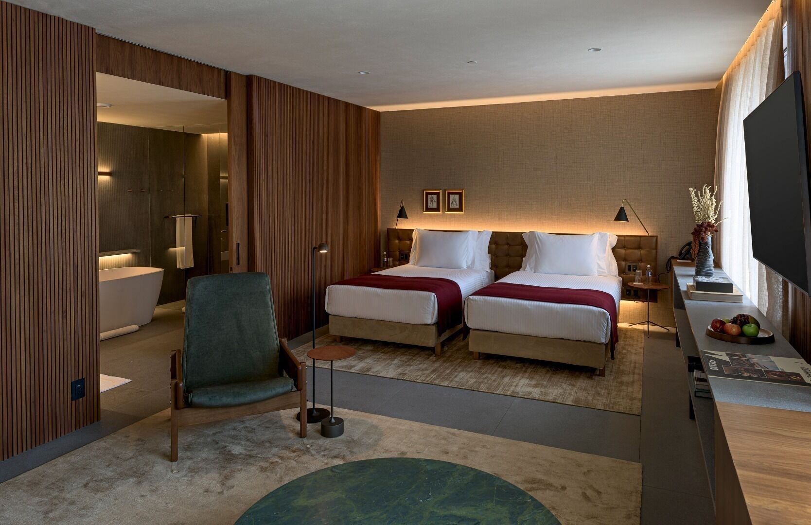 Une chambre d’hôtel moderne avec deux lits, un coin salon comprenant un fauteuil, une petite table et un téléviseur.