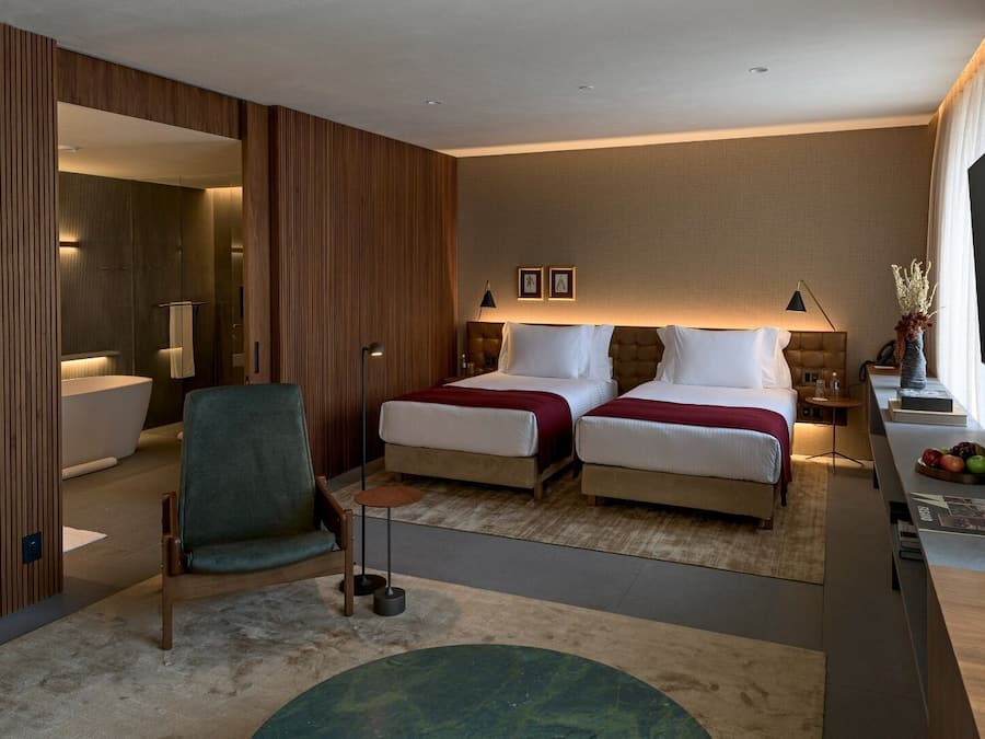 Une chambre d’hôtel moderne avec deux lits, un coin salon comprenant un fauteuil, une petite table et un téléviseur.