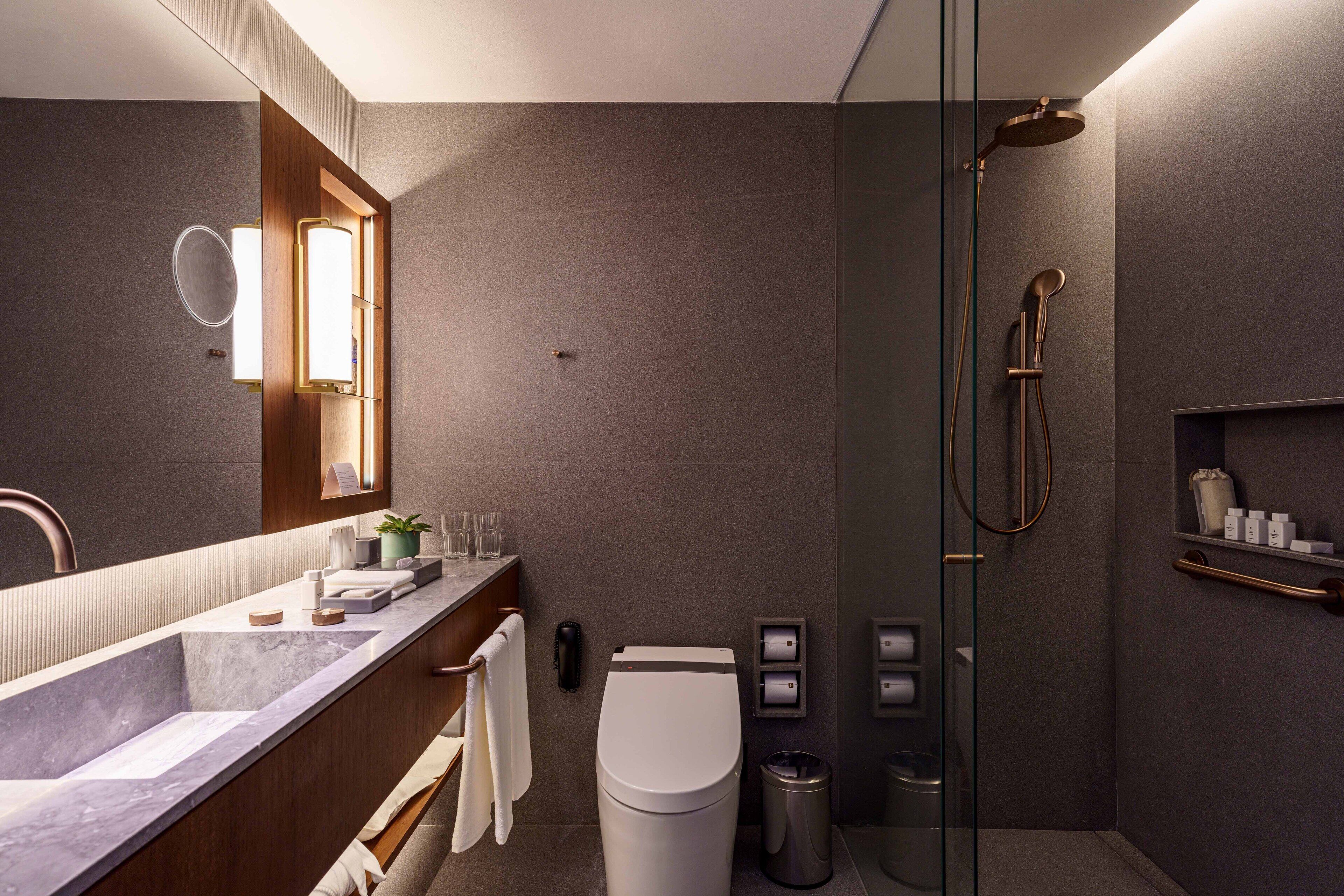 Un baño moderno con lavamanos de mármol, inodoro, ducha con mampara de vidrio y tocador con espejo y toallero.