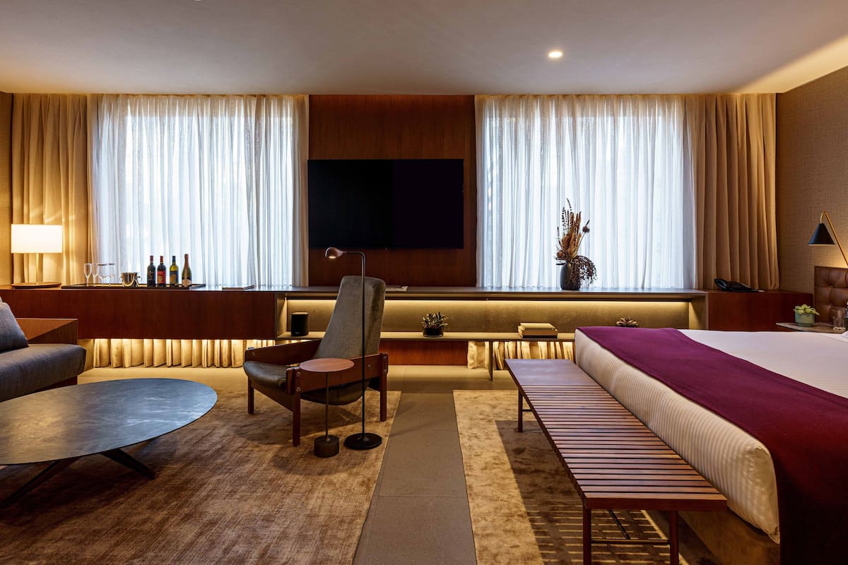 A hotel room with a bed, a sofa, a desk, a chair, a TV, and a window with curtains.