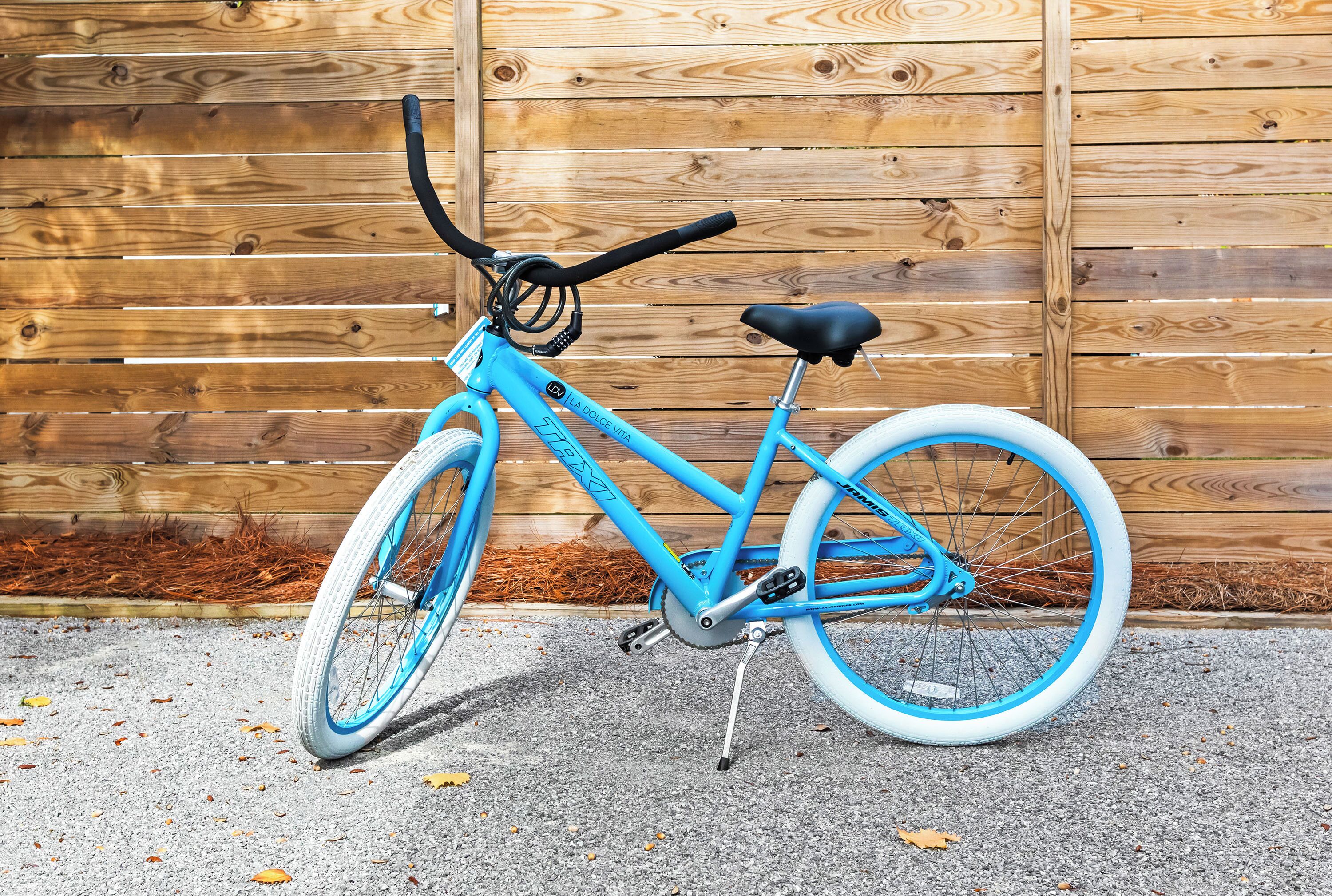 Un vélo bleu avec une selle et un guidon noirs, garé sur une surface en béton, avec une clôture en bois en arrière-plan.