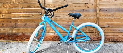 Un vélo bleu avec une selle et un guidon noirs, garé sur une surface en béton, avec une clôture en bois en arrière-plan.