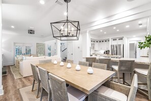 A spacious kitchen with white cabinets, a wooden dining table with six chairs, and a central chandelier. - 1 Minute to Beach, with Private Heated Pool, Carriage House, and Fire Pit (Santa Rosa Beach)