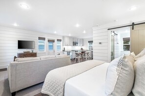 Une chambre d’hôtel moderne équipée d’un lit, de deux canapés, d’une télévision, d’un coin cuisine et d’une porte coulissante.