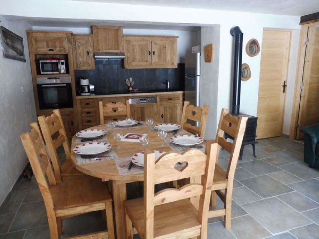 Een compacte keuken met houten kastjes, een eettafel voor vier personen en een kleine koelkast.