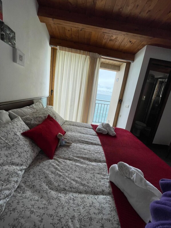 A hotel room with two beds, a wooden ceiling, a balcony with a view, and a door to the bathroom.