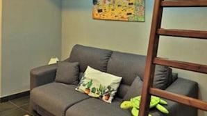 A grey sofa with a cactus pillow and a green plush toy, a wooden ladder, and a colorful abstract painting on the wall. - Apartment overlooking the sea of Cefalù (Cefalù)