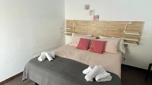 A neatly made bed with a grey and beige duvet, two pillows, and two folded white towels. - Apartment overlooking the sea of Cefalù (Cefalù)