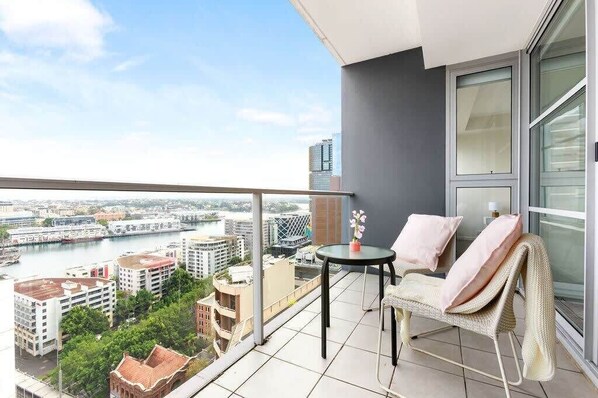 A balcony with a view of a cityscape, a table with a vase, and a chair with a blanket.