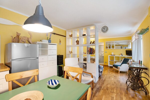 A compact living space with a dining area, kitchenette, and a small seating area with a sewing machine. - Apartment 'Il Giardino' with Lake View, Private Terrace and Wi-Fi (Belgirate)
