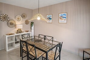A dining area with a glass table, black chairs, a woven pendant light, and wall decor including framed pictures and woven wall hangings.