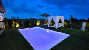 A swimming pool with a white deck, surrounded by grass and trees, with a canopy and lounge chairs in the background. - Nirvana in Halikounas (Corfu)