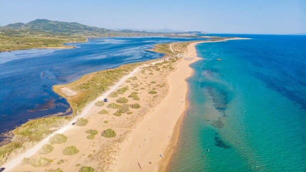 An aerial view of a coastal area with a sandy beach, clear blue waters, and a road running parallel to the shore. - Nirvana in Halikounas (Corfu)