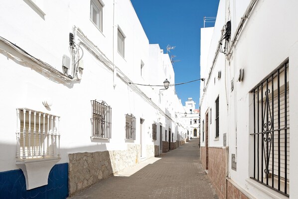A narrow street with white buildings, a stone wall, and a clear blue sky.