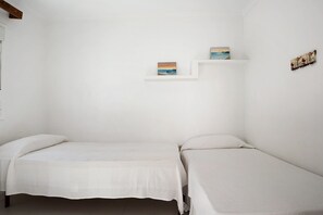 A small, white room with two single beds, a white shelf with paintings, and a white wall.