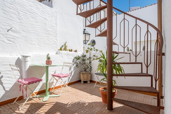 A white-walled patio with a spiral staircase, a table with chairs, and potted plants.