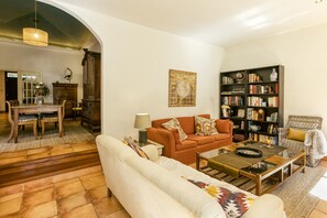 A living room with a sofa, armchair, coffee table, bookshelf, and dining area with a table and chairs. - Villa 'Maria' with Private Pool, Wi-Fi and Air Conditioning (Navata)