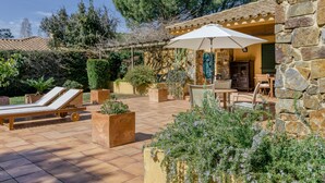 Une terrasse avec un transat, une table avec un parasol et des murs en pierre.