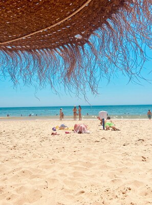 A beach with people, a straw umbrella, and beach towels.