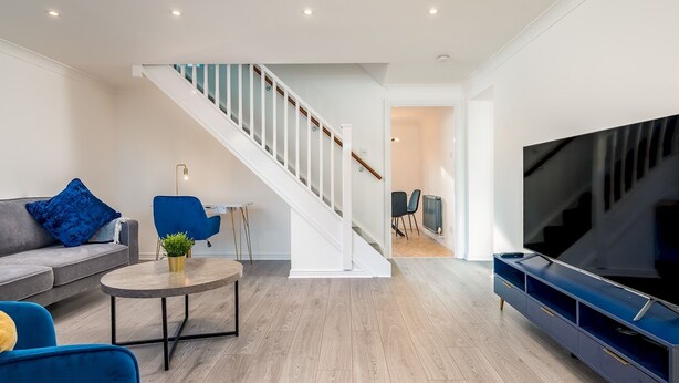 A modern living room with a staircase, a sofa, a coffee table, and a TV stand.