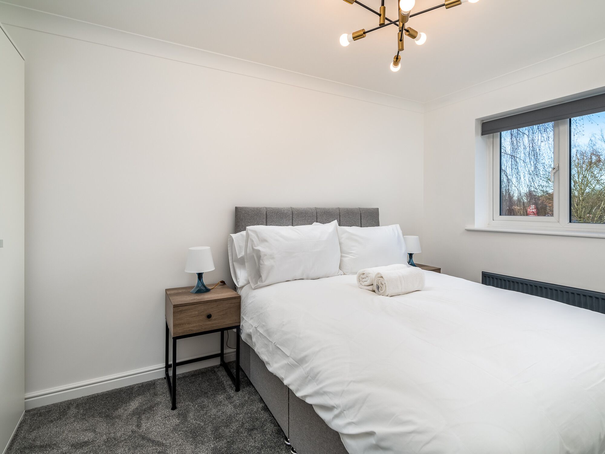 A bedroom with a bed, a nightstand, a lamp, and a window.