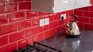 A kitchen with red tiles, a gas stove, and a kettle.