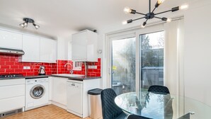 A modern kitchen with white cabinets, red backsplash, and a glass dining table with black chairs.