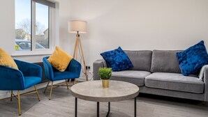 A modern living room with a grey sofa, two blue armchairs, a round coffee table, and a floor lamp.