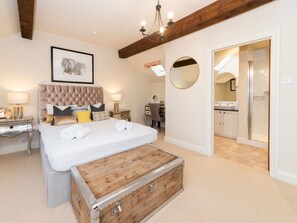 A bedroom with a large bed, a chest of drawers, a bedside table, a desk, a chair, a mirror, and a bathroom visible through an open door.