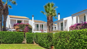 A row of white villas with tiled roofs, surrounded by well-maintained hedges and palm trees. - Holiday Home 'Aloes' with Shared Pool, Private Terrace and Wi-Fi (Ciutadella de Menorca)