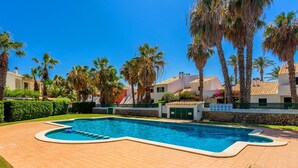A swimming pool with a tiled deck, surrounded by palm trees and a stone wall. - Holiday Home 'Aloes' with Shared Pool, Private Terrace and Wi-Fi (Ciutadella de Menorca)