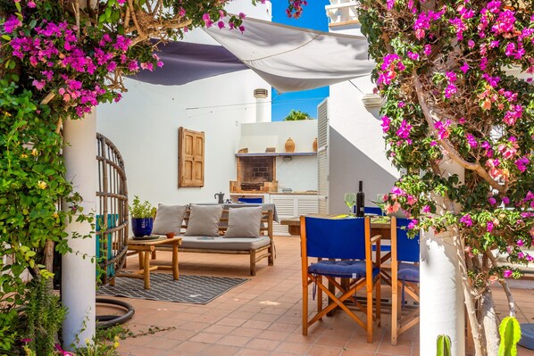 A patio with a wooden table and chairs, a cushioned bench, and potted plants.