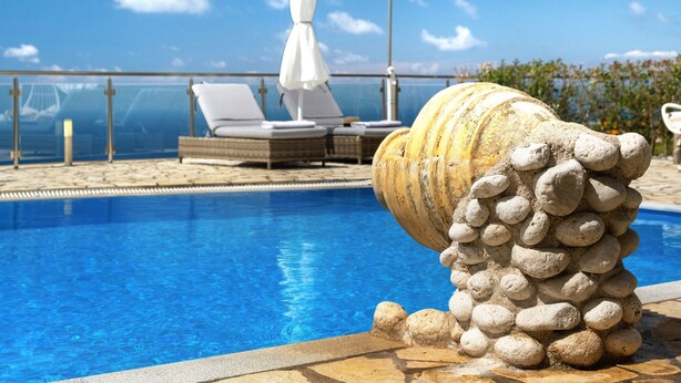 Une piscine agrémentée d’une sculpture en pierre, de chaises longues et d’un parasol blanc.