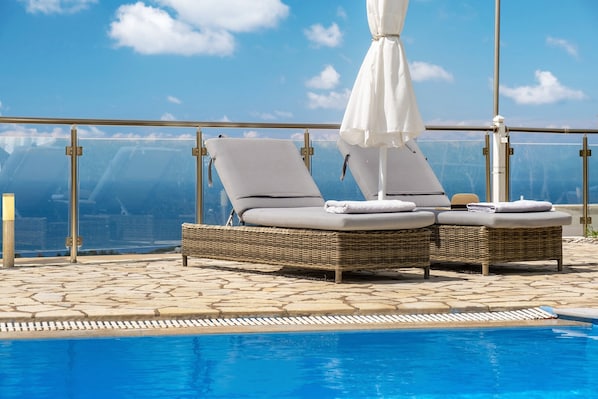 Un espace aménagé au bord de la piscine, avec deux fauteuils de relaxation en osier, un parasol blanc et une vue dégagée sur l’océan.