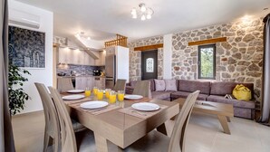 Une cuisine moderne avec un mur en pierre, un coin repas avec une table et des chaises en bois, et un salon avec un canapé et une fenêtre.