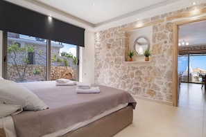 Une chambre avec un grand lit, des murs en pierre, une vue sur l’extérieur et un balcon.