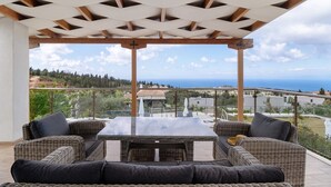 Un espace extérieur aménagé, abrité et doté de mobilier en osier, offrant une vue sur la mer.