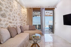 A living room with a stone wall, a sofa set, a glass coffee table, and a view through a glass door. - Holiday Apartment "Suite Irida" with Sea View, 2 Terraces & Wi-Fi (Lefkada)