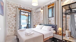 A bedroom with a bed, bedside table, lamp, and a view through a window. - Holiday Apartment "Suite Irida" with Sea View, 2 Terraces & Wi-Fi (Lefkada)