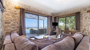 Una sala de estar con una pared de piedra, un sofá, un televisor y vista al mar.