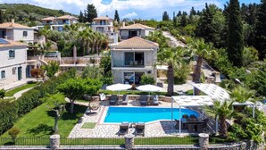 Una villa con piscina, mobiliario exterior y un camino de piedra.