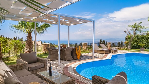 Zona junto a la piscina con mobiliario de mimbre, una mesa de vidrio y vistas al mar.